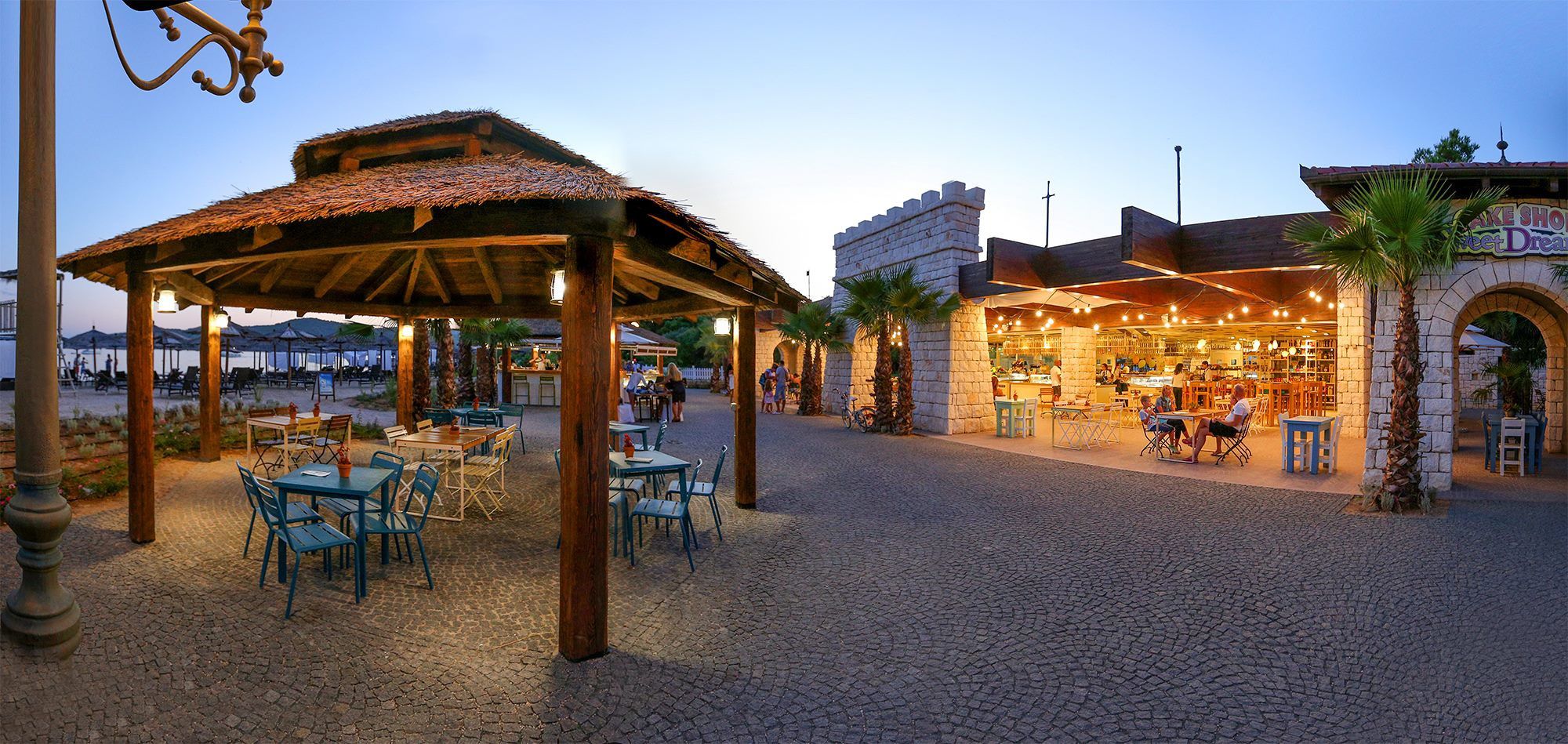 An outdoor dining area with tables and chairs, a covered seating area, and a building with a stone facade.