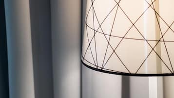 A modern lamp with a geometric pattern on its shade, positioned against a backdrop of vertical blinds.