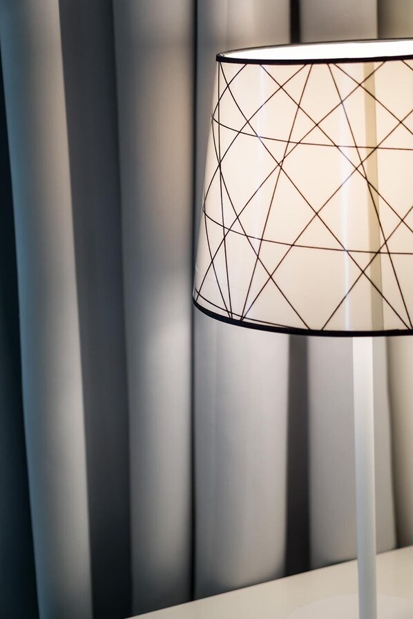 A modern lamp with a geometric pattern on its shade, positioned against a backdrop of vertical blinds.