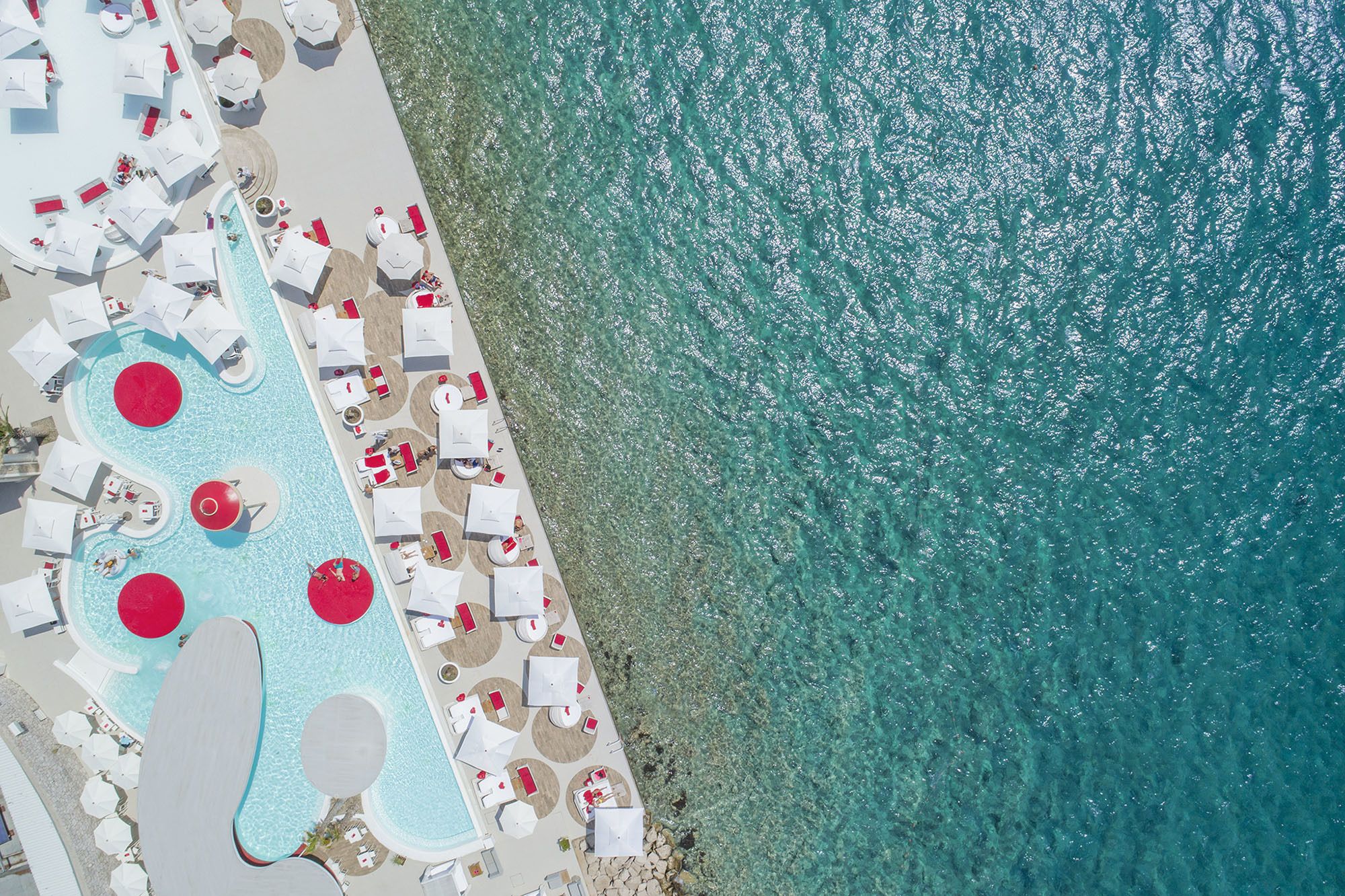 Vue aérienne d’un complexe hôtelier avec une piscine, des chaises longues et des parasols.