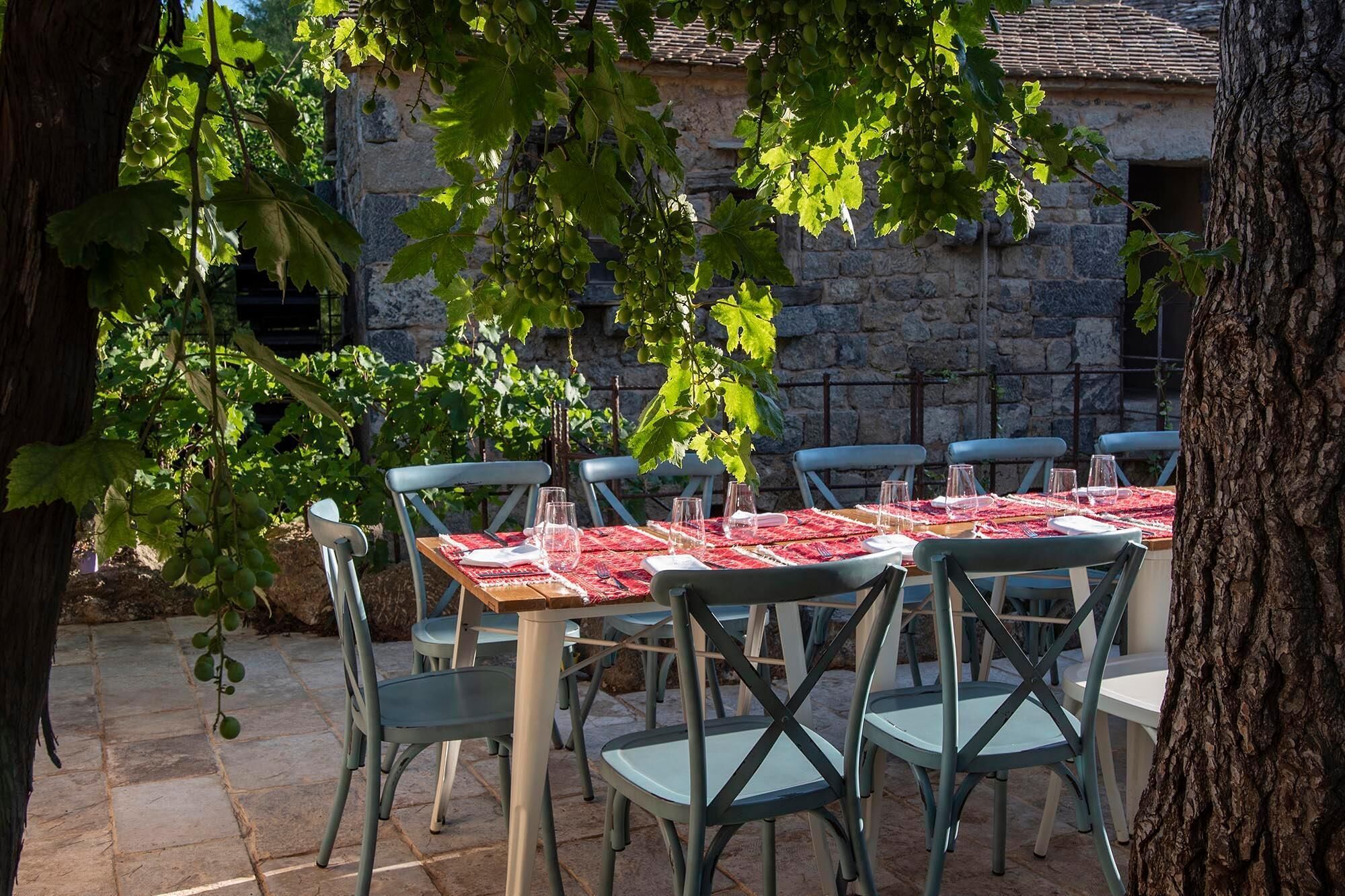 An outdoor dining area with stone walls, green chairs, and a table set for six with red tablecloths.