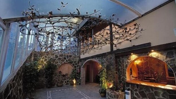 A spacious interior with a stone wall, a fireplace, and a ceiling with hanging branches. - Hotel Reino Nevado (Monachil)