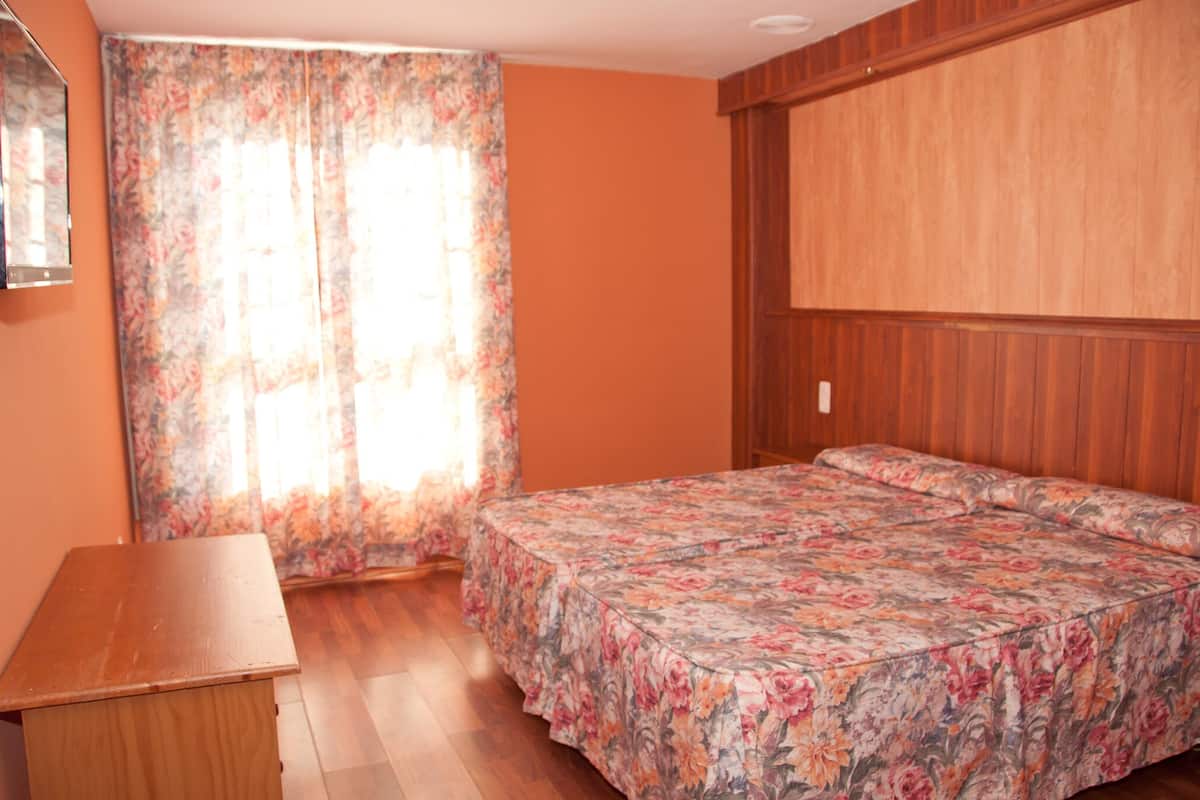 A bedroom with a wooden bed, a wooden nightstand, and a window with floral curtains.