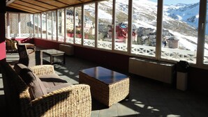 A cozy lounge area with wicker furniture, large windows offering a view of a snowy mountain landscape. - Hotel Reino Nevado (Monachil)