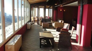 A spacious indoor area with large windows, wicker furniture, and a wooden ceiling. - Hotel Reino Nevado (Monachil)