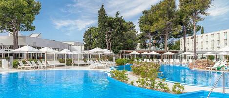 Ein Swimmingpool mit Liegestühlen und Sonnenschirmen, umgeben von Bäumen und einem Gebäude.
