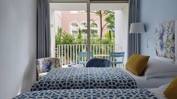 A hotel room with a balcony, a bed with patterned bedding, a chair, a table, and a lamp.