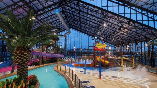 Ein Wasserpark im Innenbereich mit Rutschen, einem Schwimmbecken und tropischem Ambiente.