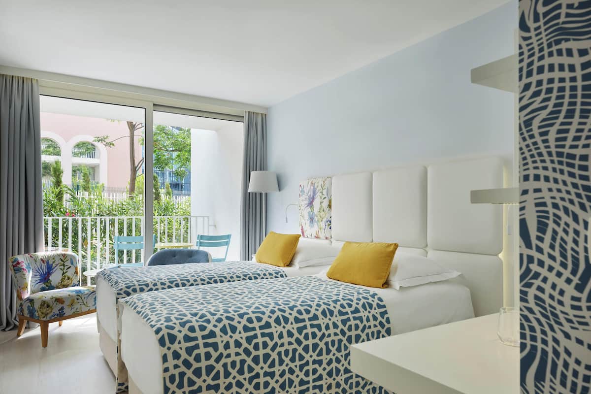 Ein Hotelzimmer mit zwei Betten, einem Balkon mit Blick, einem kleinen Tisch und einem Stuhl.