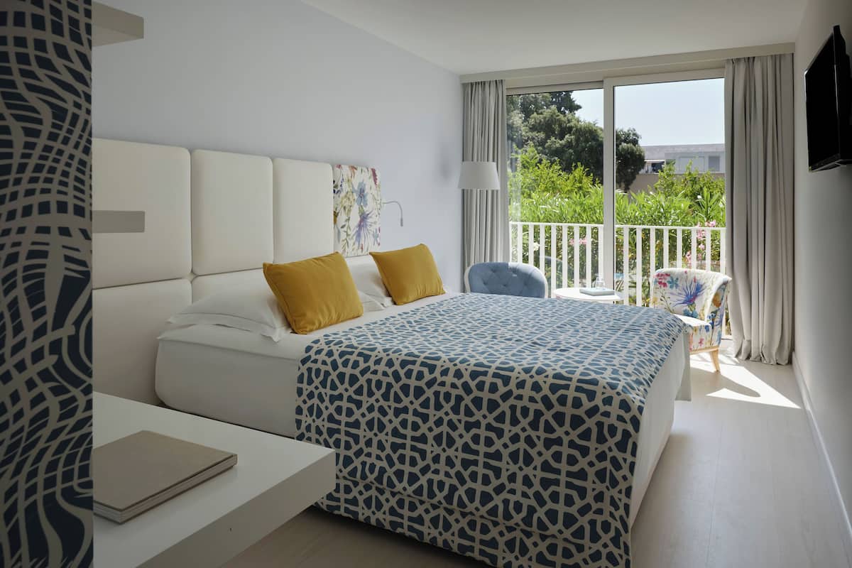 Ein Hotelzimmer mit Bett, Schreibtisch, Stuhl und einem Balkon mit Blick.