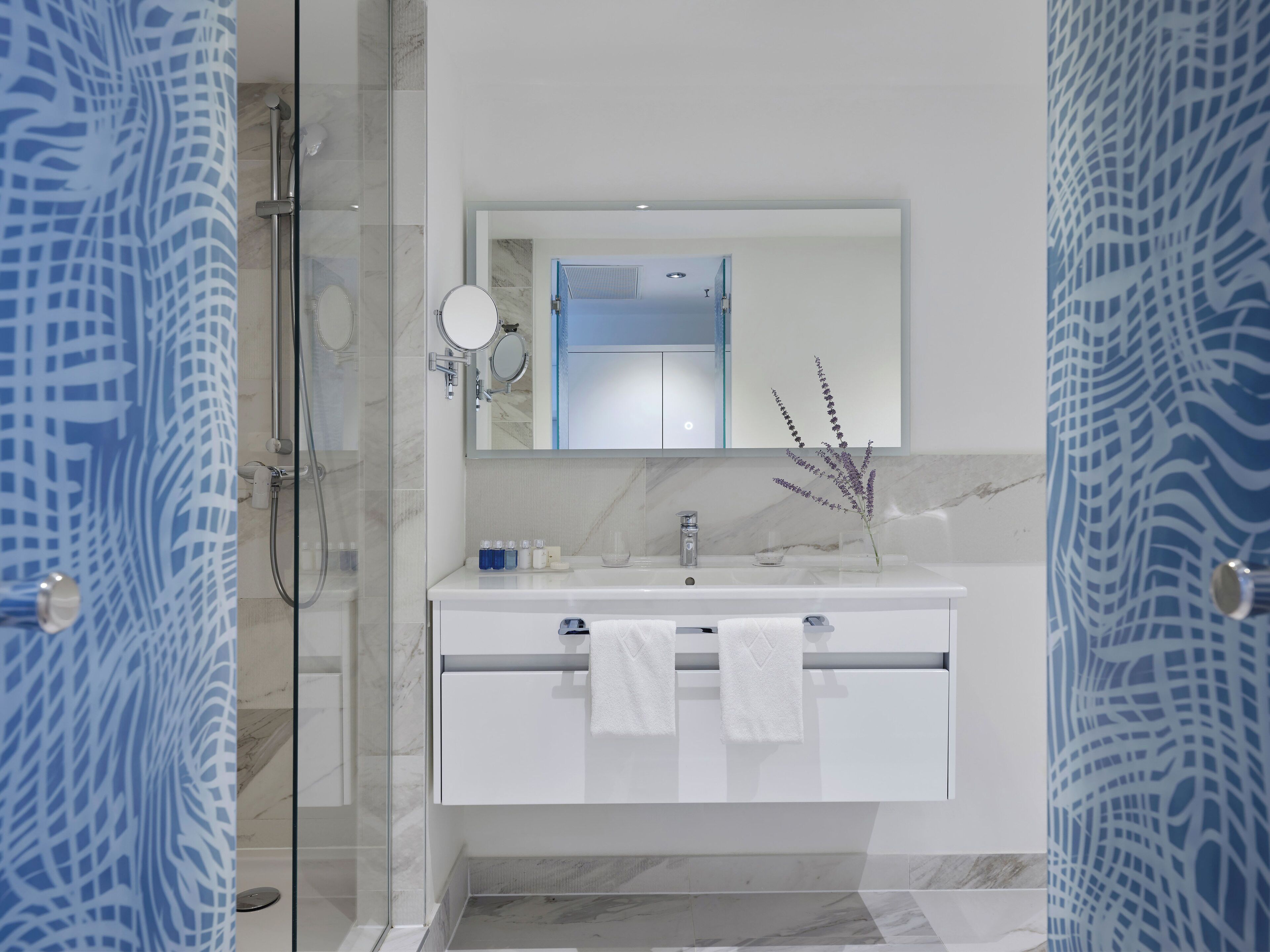 A modern bathroom with a glass shower enclosure, a white vanity with a mirror, and a decorative plant.