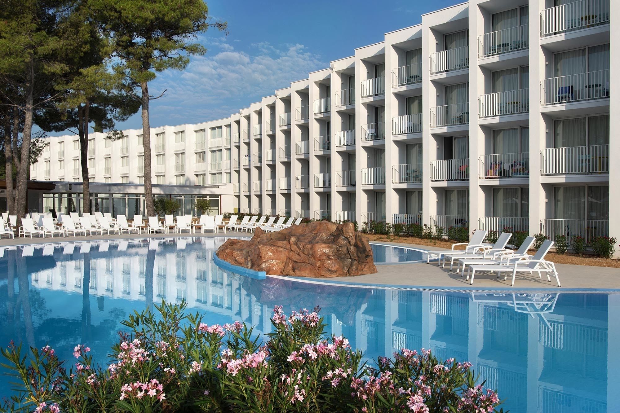 Ein Hotel mit Pool, weißen Balkonen und Liegestühlen.