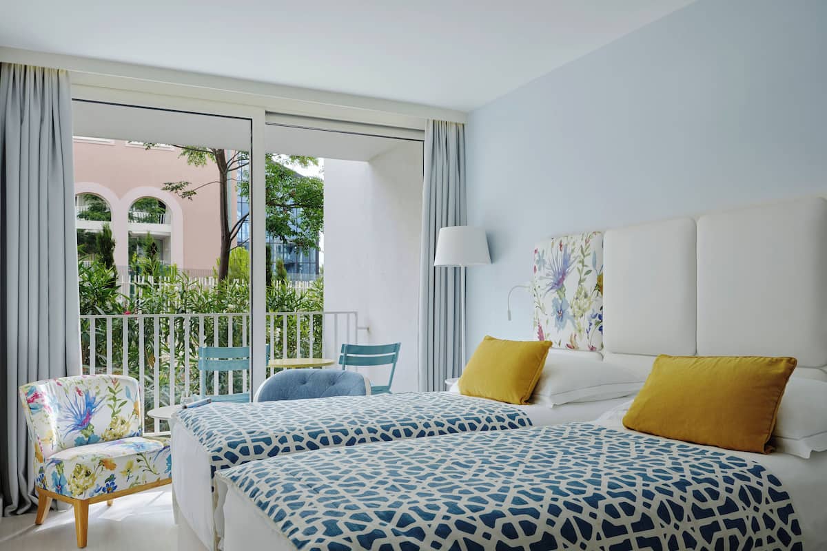 Ein Hotelzimmer mit zwei Betten, einem Balkon, einem Stuhl und einem Tisch.