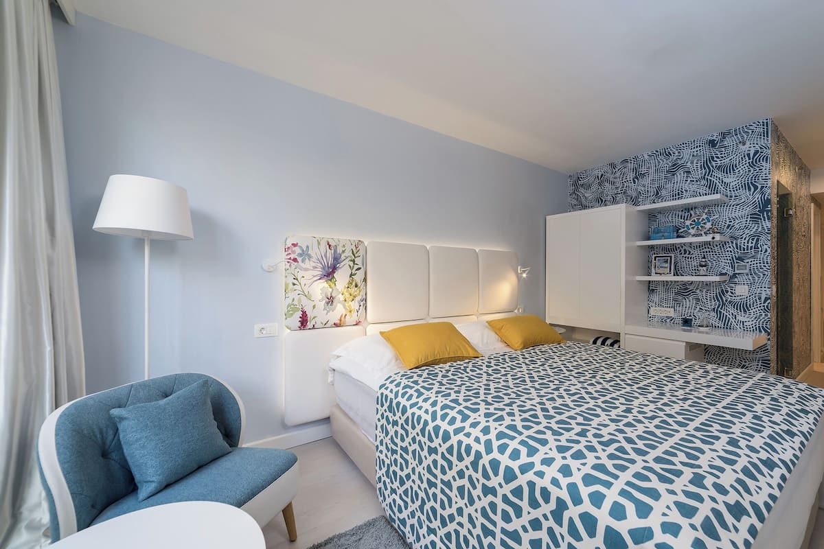 Ein modernes Hotelzimmer mit Bett, Sessel, Schreibtisch und Kleiderschrank.