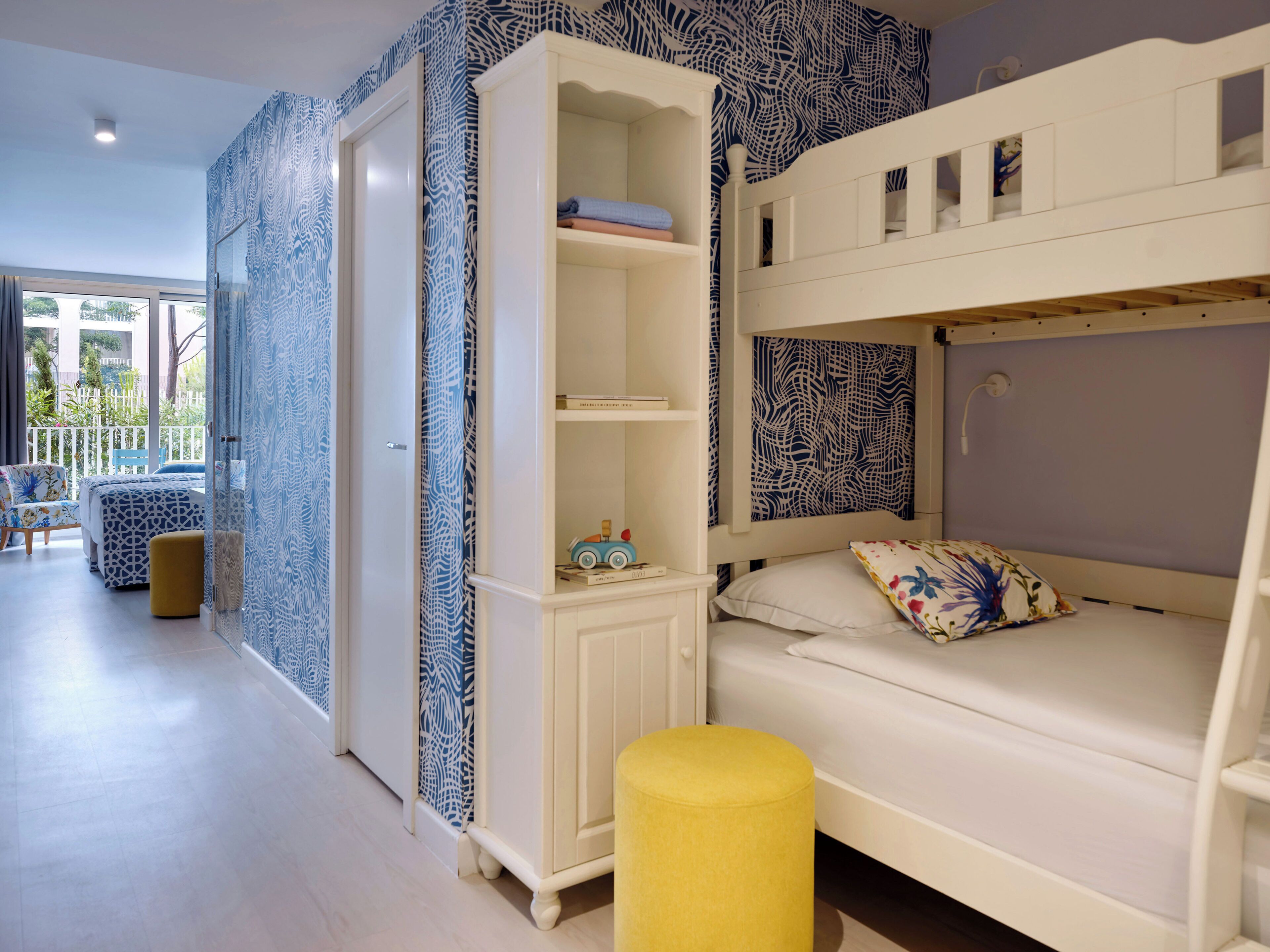 A room with a bunk bed, a wardrobe, a small table, and a window with a view of the outside.