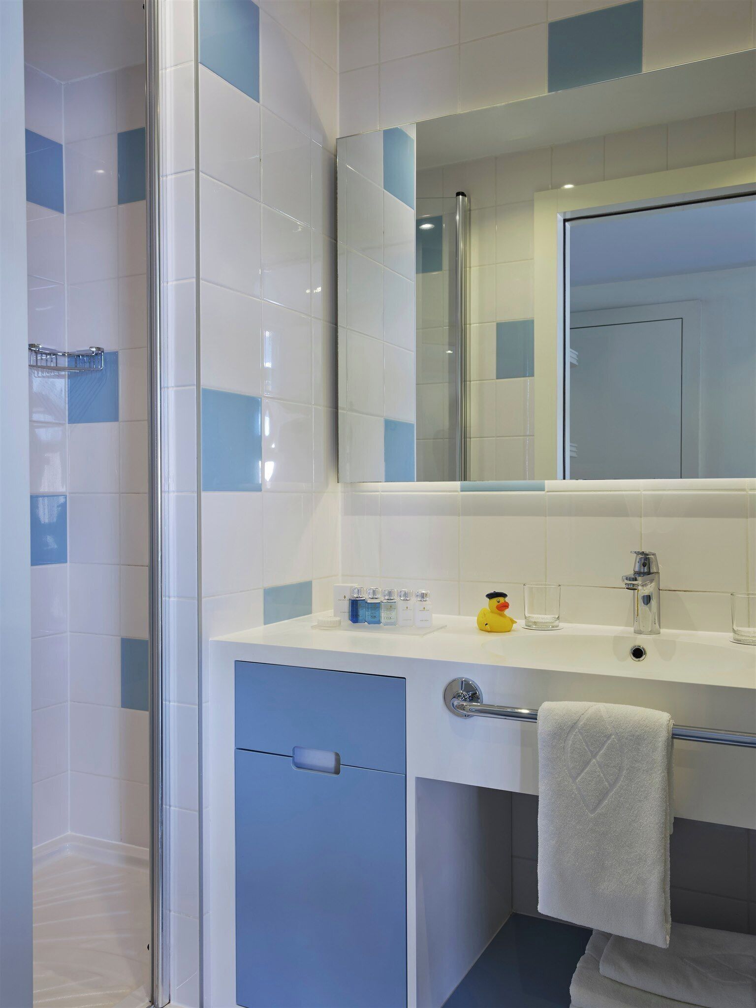 Un baño moderno con cabina de ducha de vidrio, un lavabo blanco con espejo y un perchero con una toalla blanca.