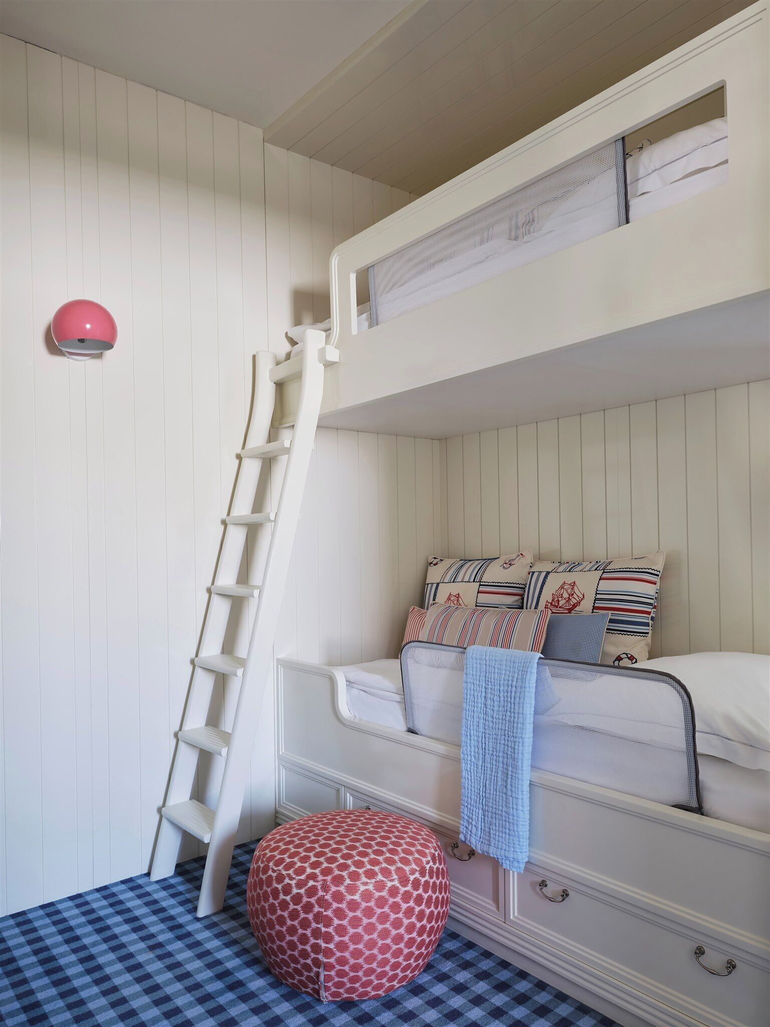 A bunk bed with a ladder, a checkered floor, and a patterned ottoman.