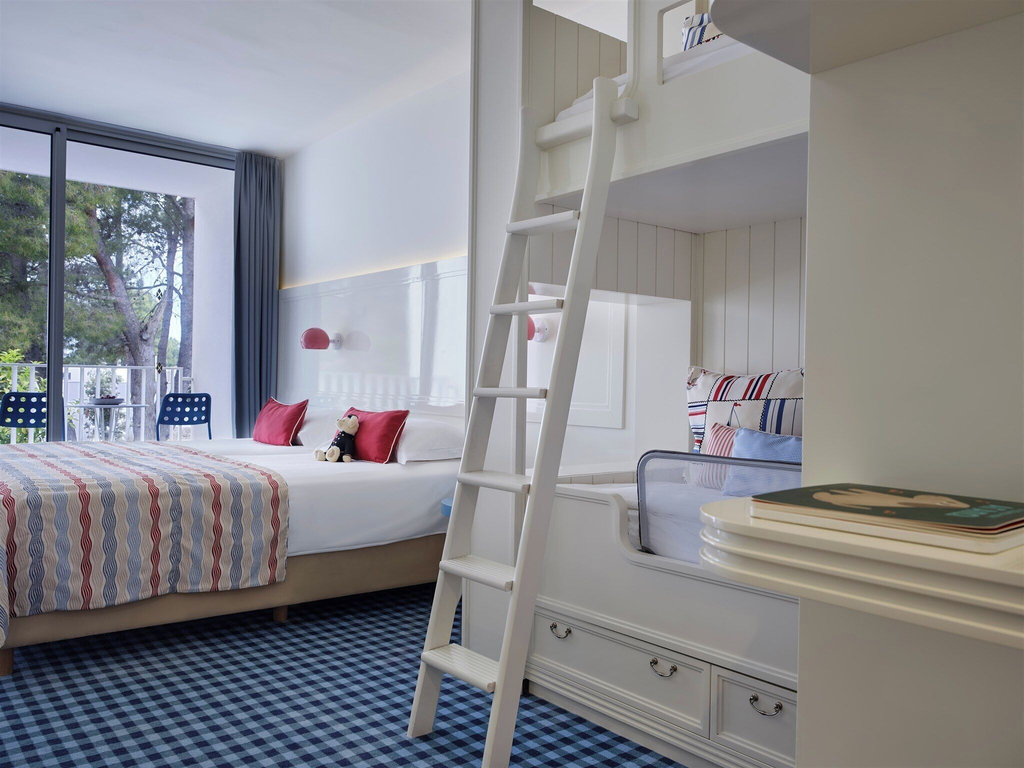 Ein Schlafzimmer mit einem Bett, einer Leiter, einem Schreibtisch und einem Fenster mit Blick auf Bäume.