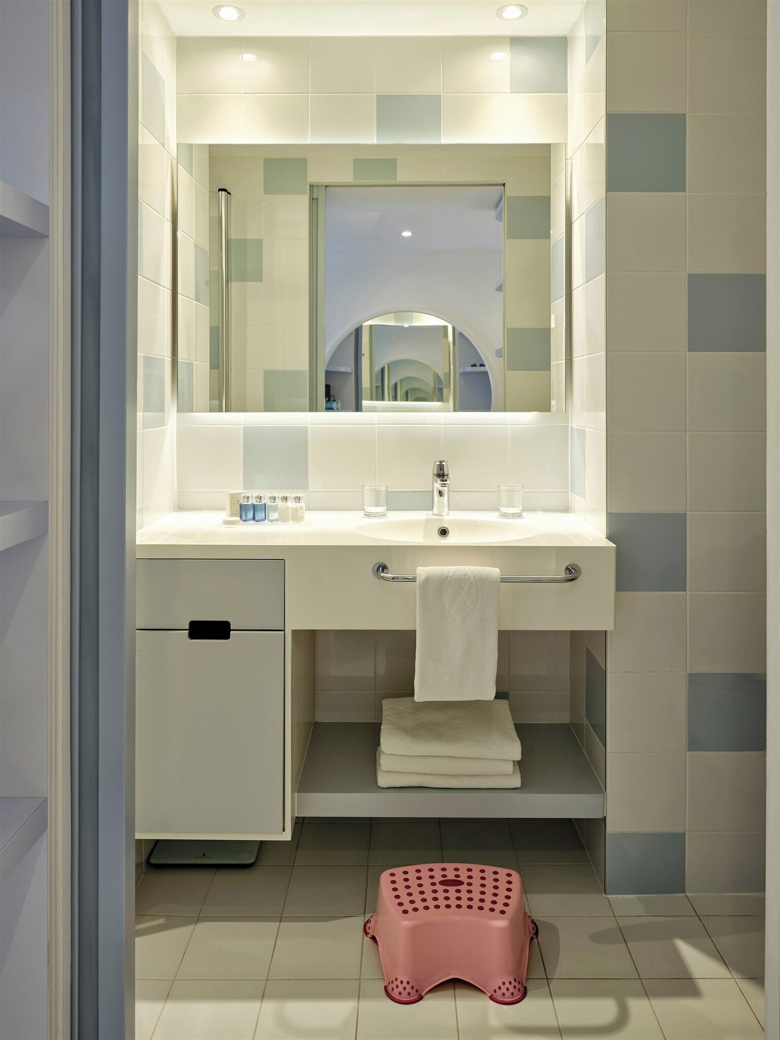 A modern bathroom with a white sink, mirror, and tiled walls.