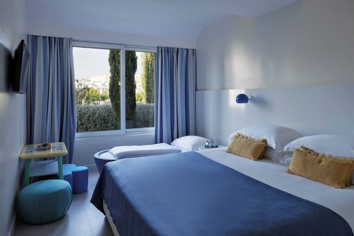 A hotel room with two beds, a small table, and a window with curtains.