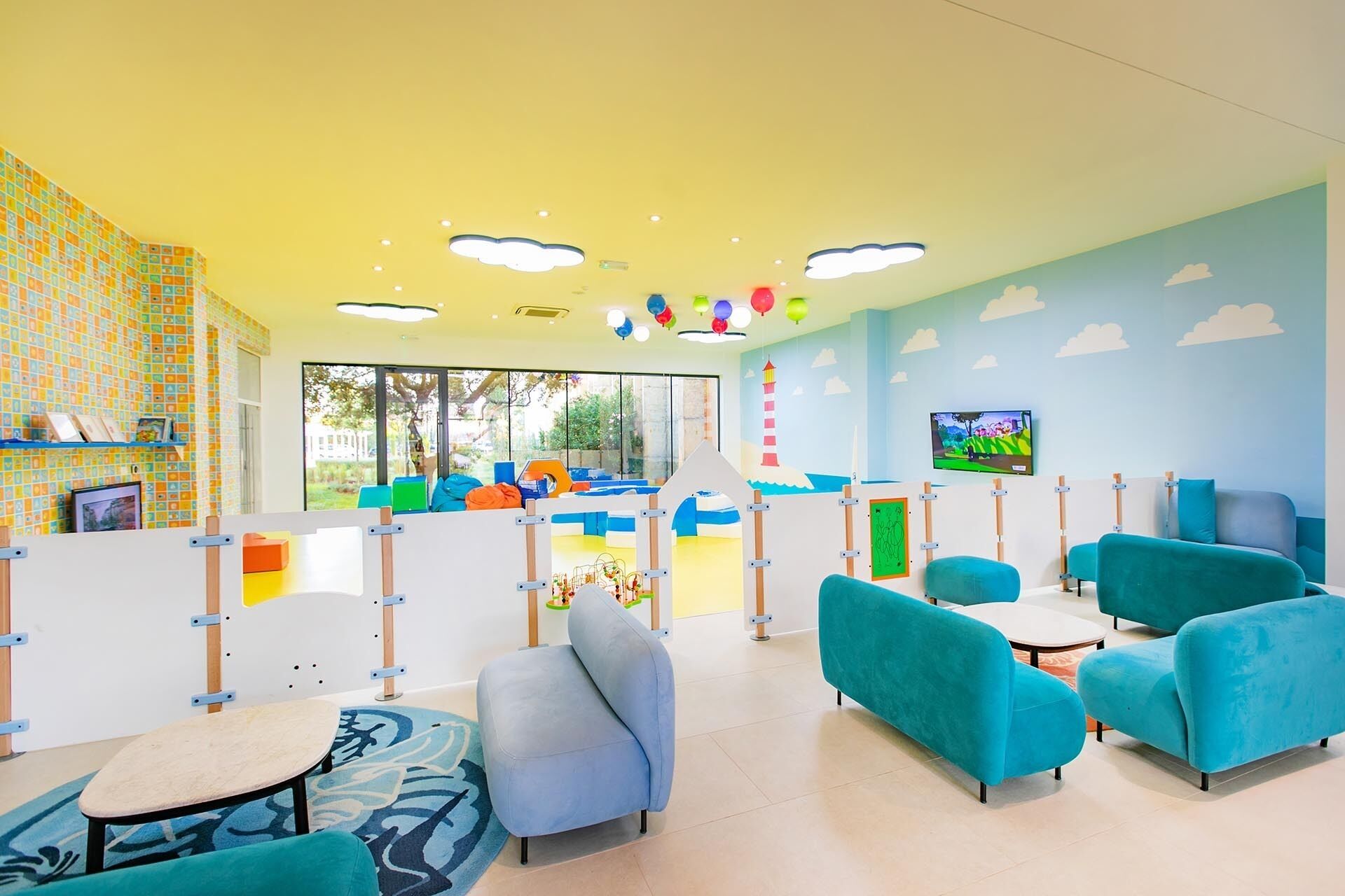 Un espace de jeux pour enfants aux couleurs vives, équipé de sièges et d’un téléviseur.