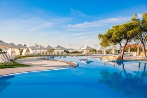 A swimming pool with lounge chairs and umbrellas, surrounded by a landscaped area with trees and a clear sky. - Amadria Park Kids Hotel Andrija (Sibenik)