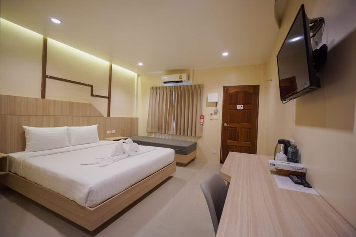 A hotel room with a bed, a desk, a television, and an air conditioning unit.