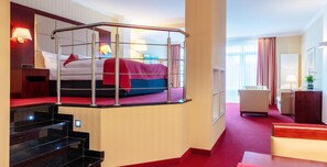 Habitación de hotel con literas, un escritorio, una silla, una lámpara y una ventana con cortinas.