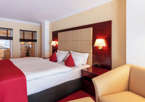 A hotel room with a large bed, two bedside lamps, a red throw blanket, and a wooden headboard. - Hotel Amaris Bremerhaven (Bremerhaven)