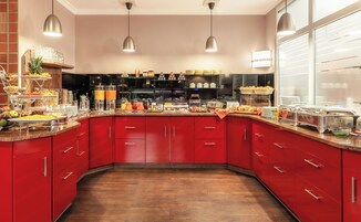 Una cocina moderna con armarios rojos, diversas opciones de comida a la vista e iluminación colgante.
