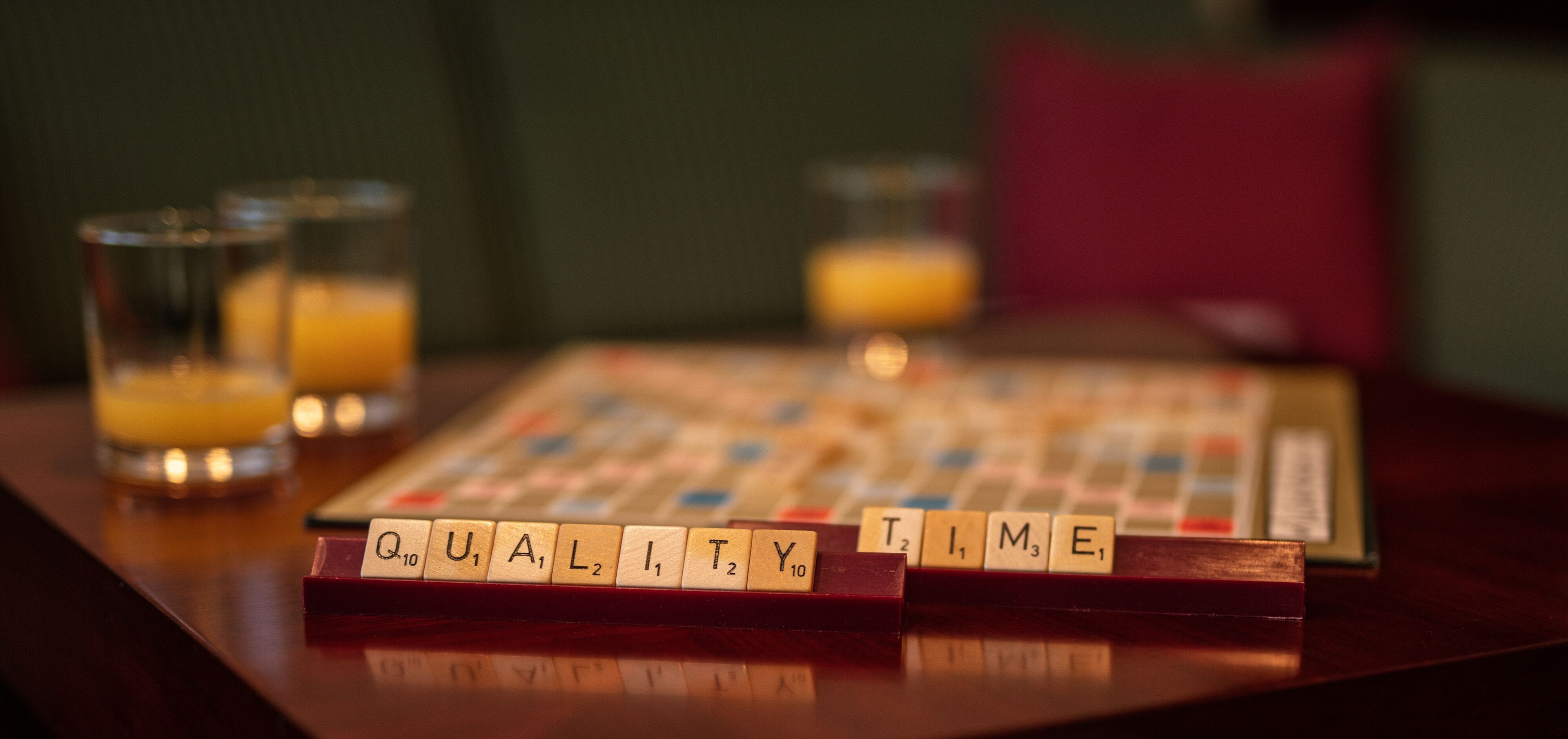 Un juego de Scrabble sobre una mesa de madera con vasos de jugo de naranja.