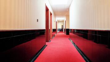 Un pasillo de hotel con piso de moqueta roja, paredes blancas y detalles en negro.