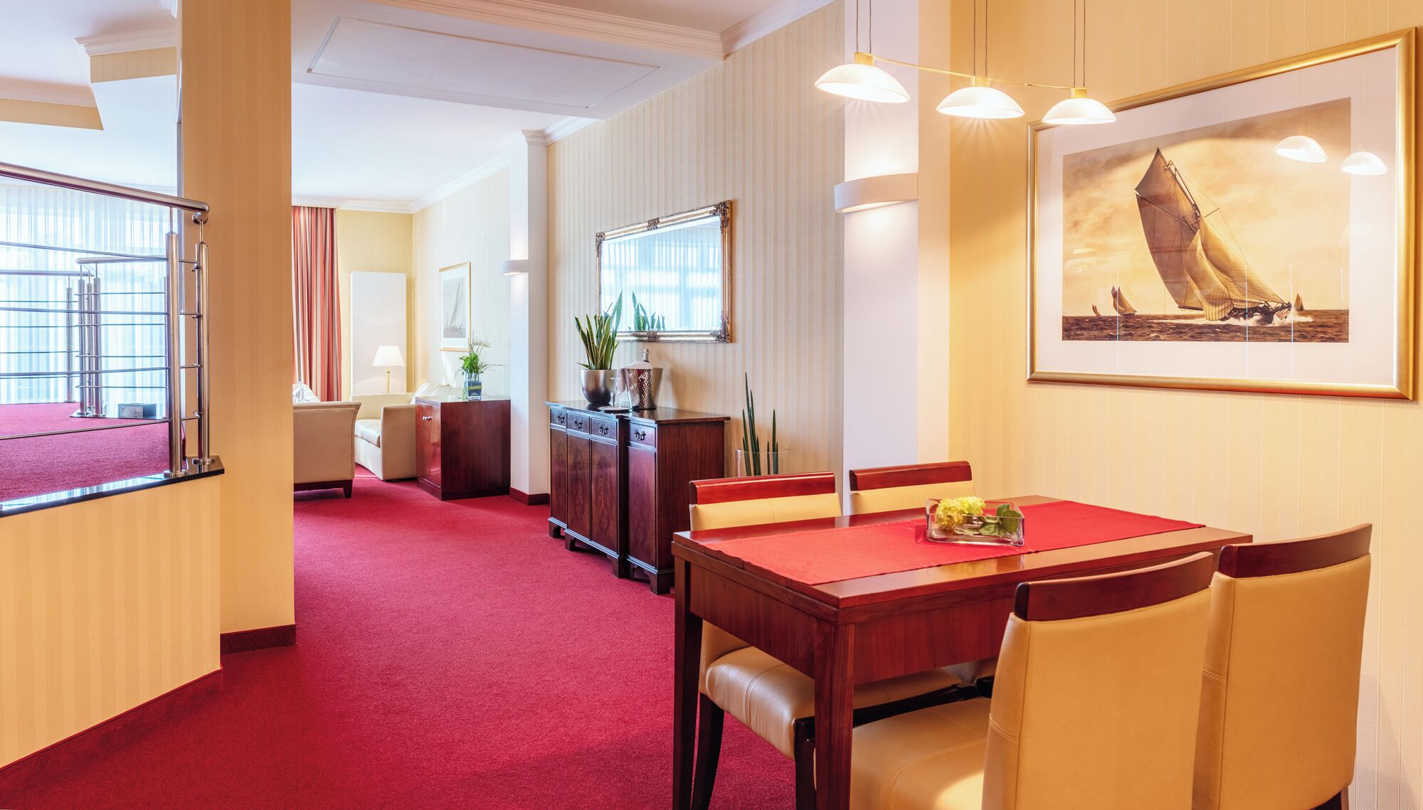 A hotel room with a dining area, a large window with curtains, a mirror, and a framed painting of a sailboat.