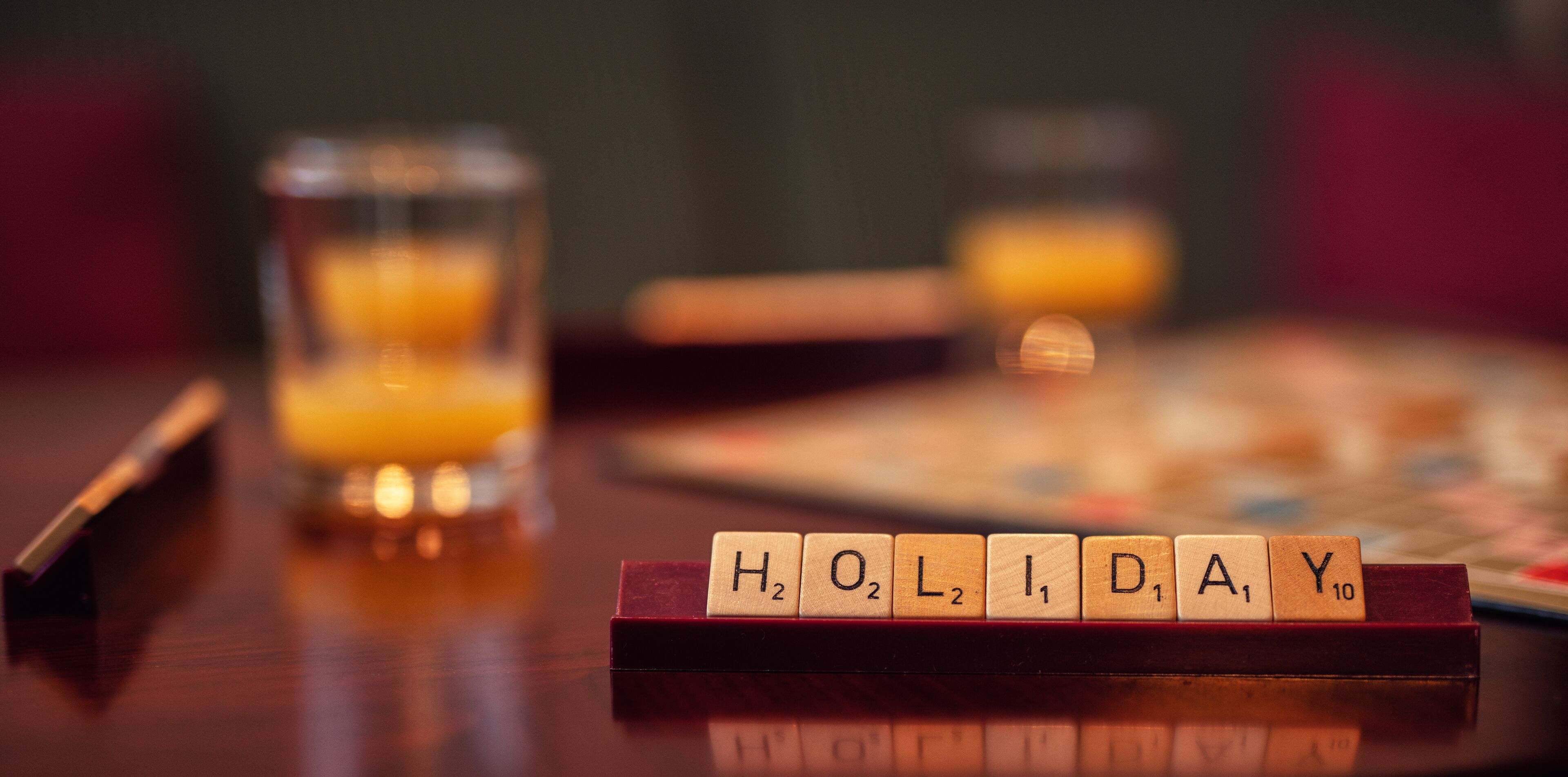 A close-up of Scrabble tiles spelling out "H2O," "L2," "I1," "D1," "A1," and "Y10" on a wooden surface.