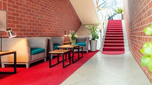 A modern lobby with a red carpet, a staircase, and seating areas with teal cushions. -  Hotel Amaris Bremerhaven (Bremerhaven)