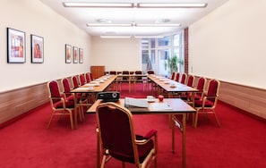 Un salón de conferencias con una larga mesa, sillas rojas y cuadros en las paredes.