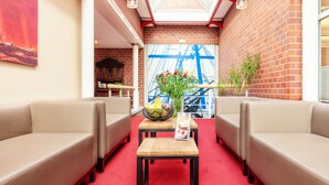 A cozy lounge area with leather sofas, a wooden table with a fruit bowl, and a red carpet. - Hotel Amaris Bremerhaven (Bremerhaven)