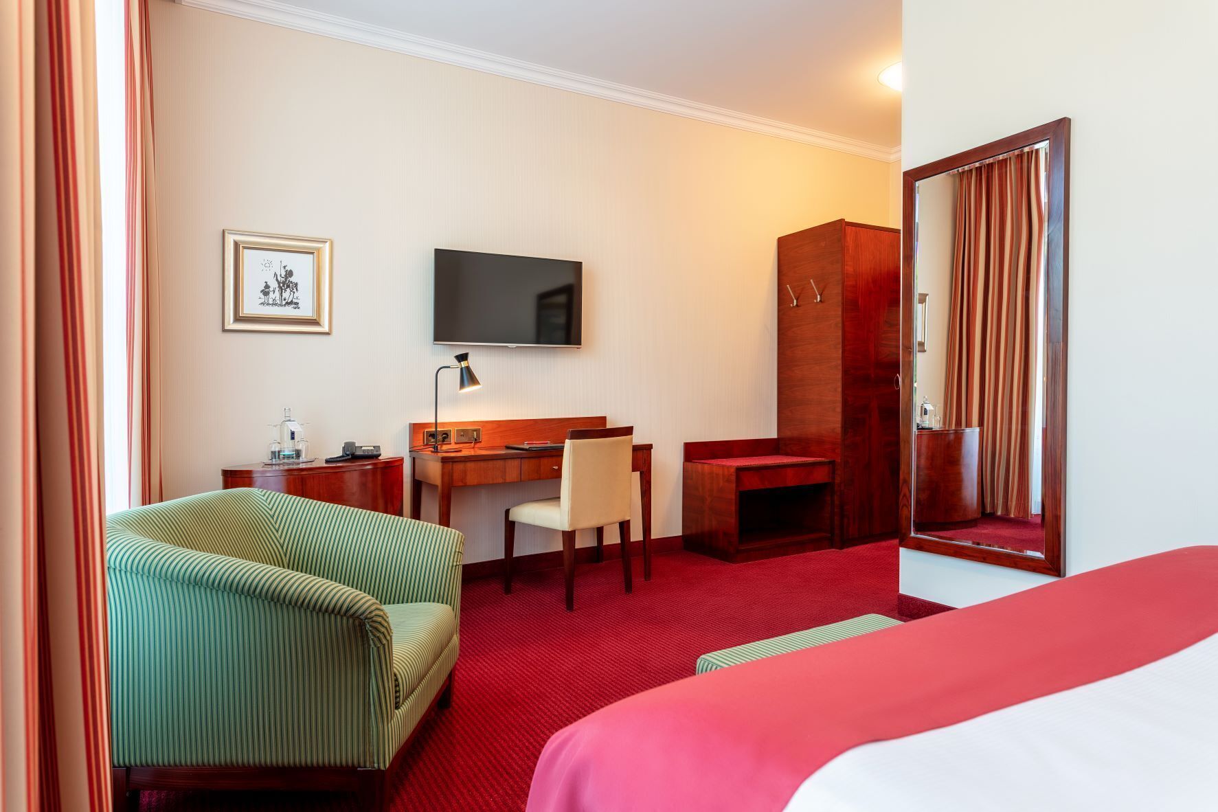 A hotel room with a bed, a desk, a chair, a television, a mirror, and a window with curtains.