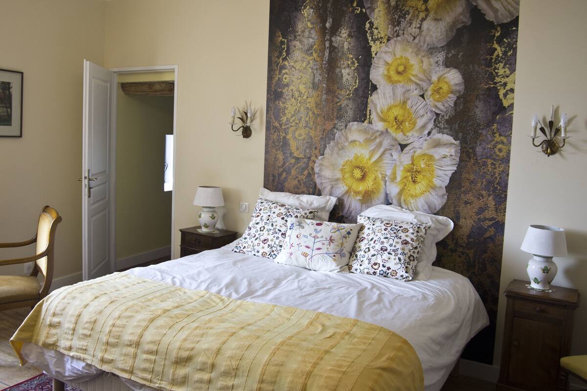 A bedroom with a bed, a chair, a nightstand, and a wall tapestry.
