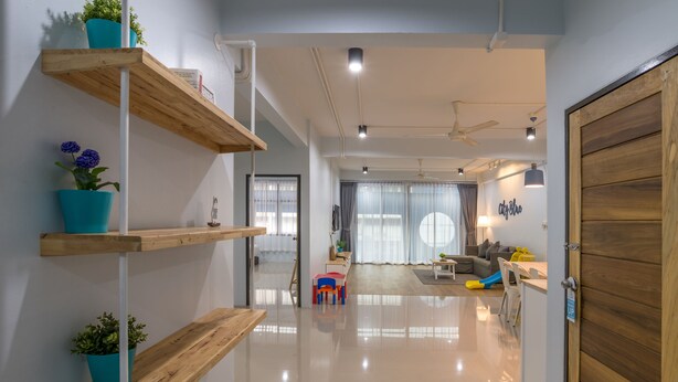 A modern interior with wooden shelves, a polished floor, and a view into a living area with a sofa and curtains. - Otter House (Krabi)