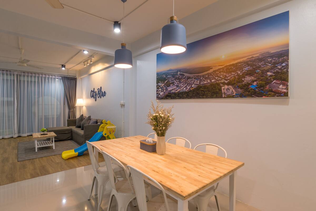 A modern living room with a dining area, featuring a large cityscape painting, a wooden dining table, and a sofa with a city-themed wall art.