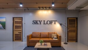 A modern room with a large sign reading "SKY LOFT," a leather sofa, a small table with a plant and book, and a lamp. - Otter House (Krabi)