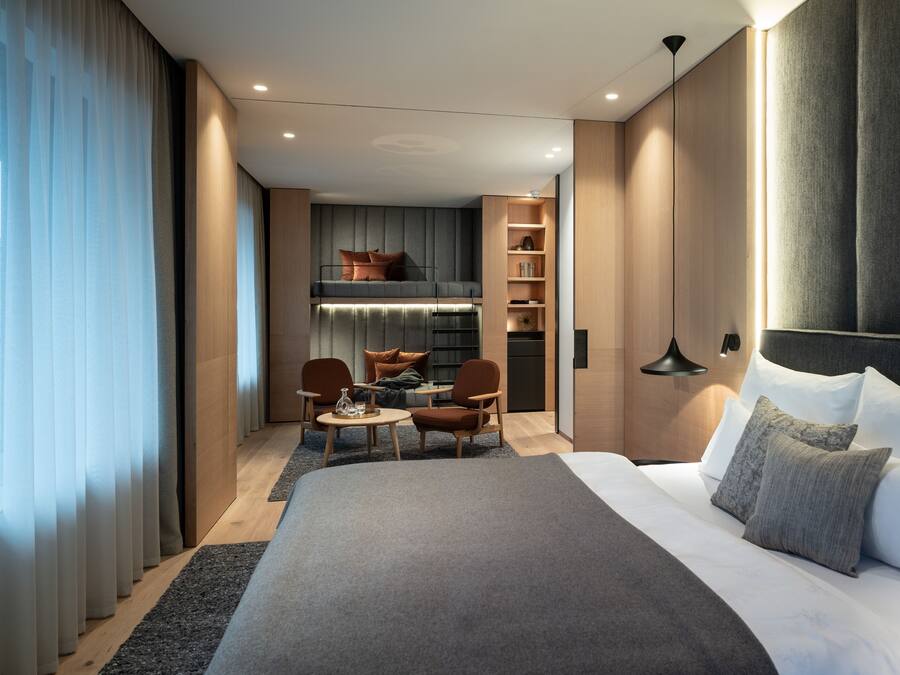 Quarto de hotel moderno com uma cama grande, uma mesa com cadeiras, uma kitchenette e um guarda-roupa.