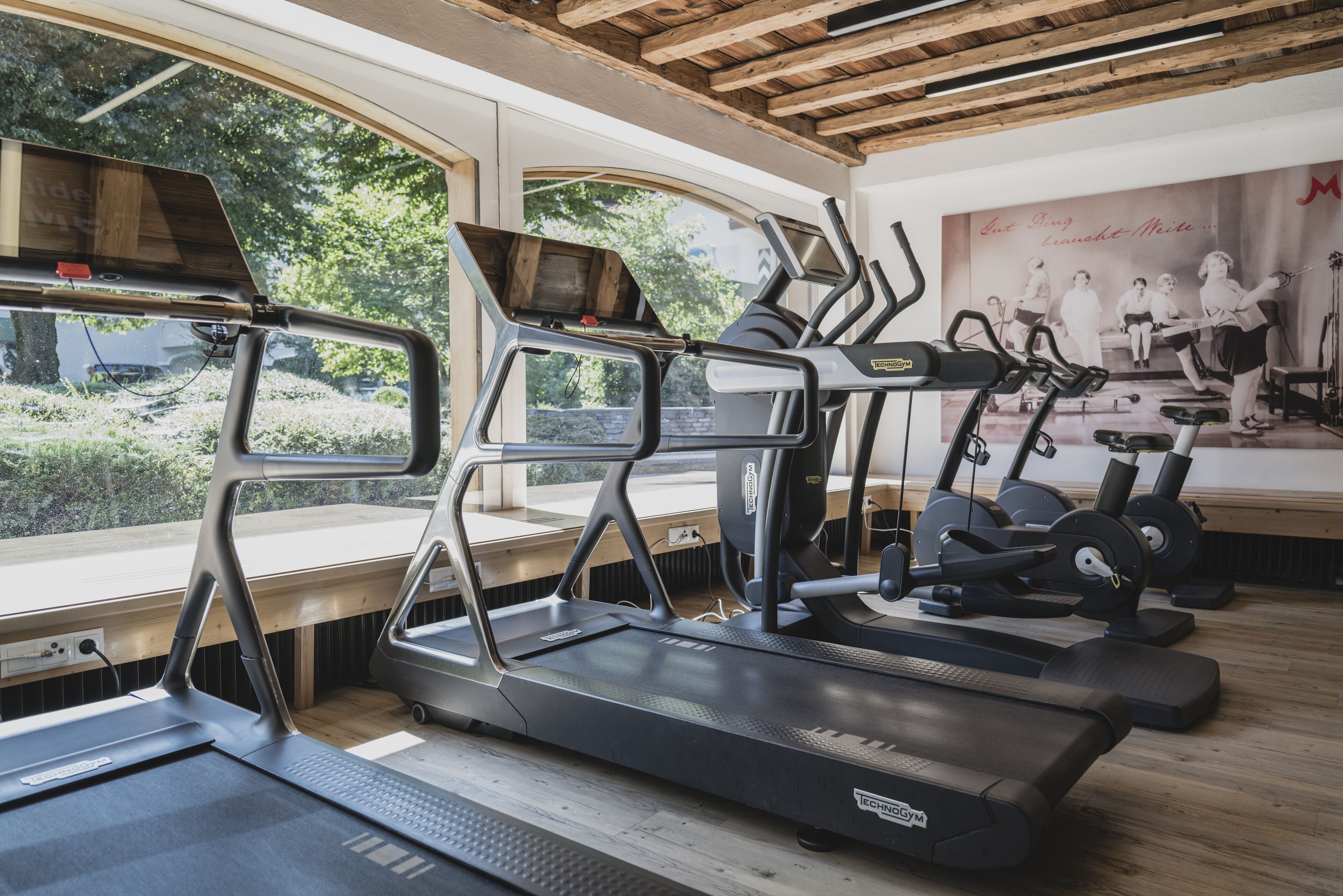 A gym with treadmills, exercise bikes, and a large window overlooking greenery.