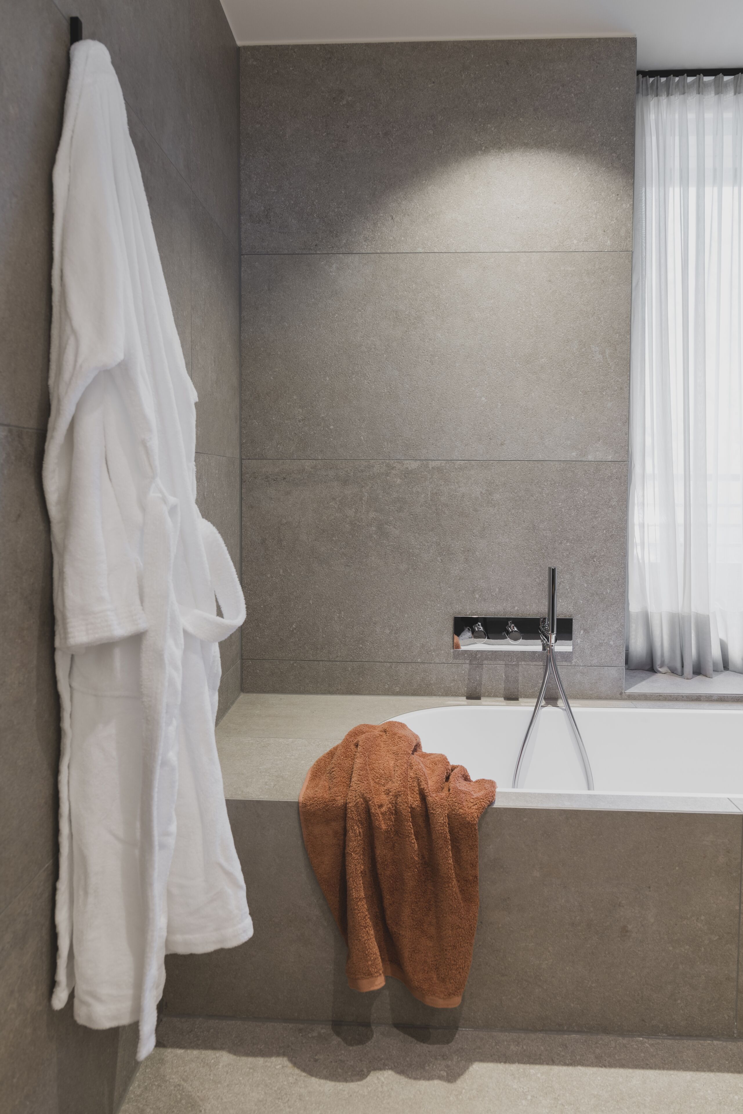 Un baño moderno con una bañera, un perchero con una toalla blanca y otra toalla marrón en el suelo.