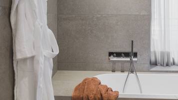 Une salle de bain moderne avec une baignoire, un porte-serviettes sur lequel est posée une serviette blanche, et une serviette marron sur le sol.
