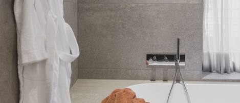 Un baño moderno con una bañera, un perchero con una toalla blanca y otra toalla marrón en el suelo.