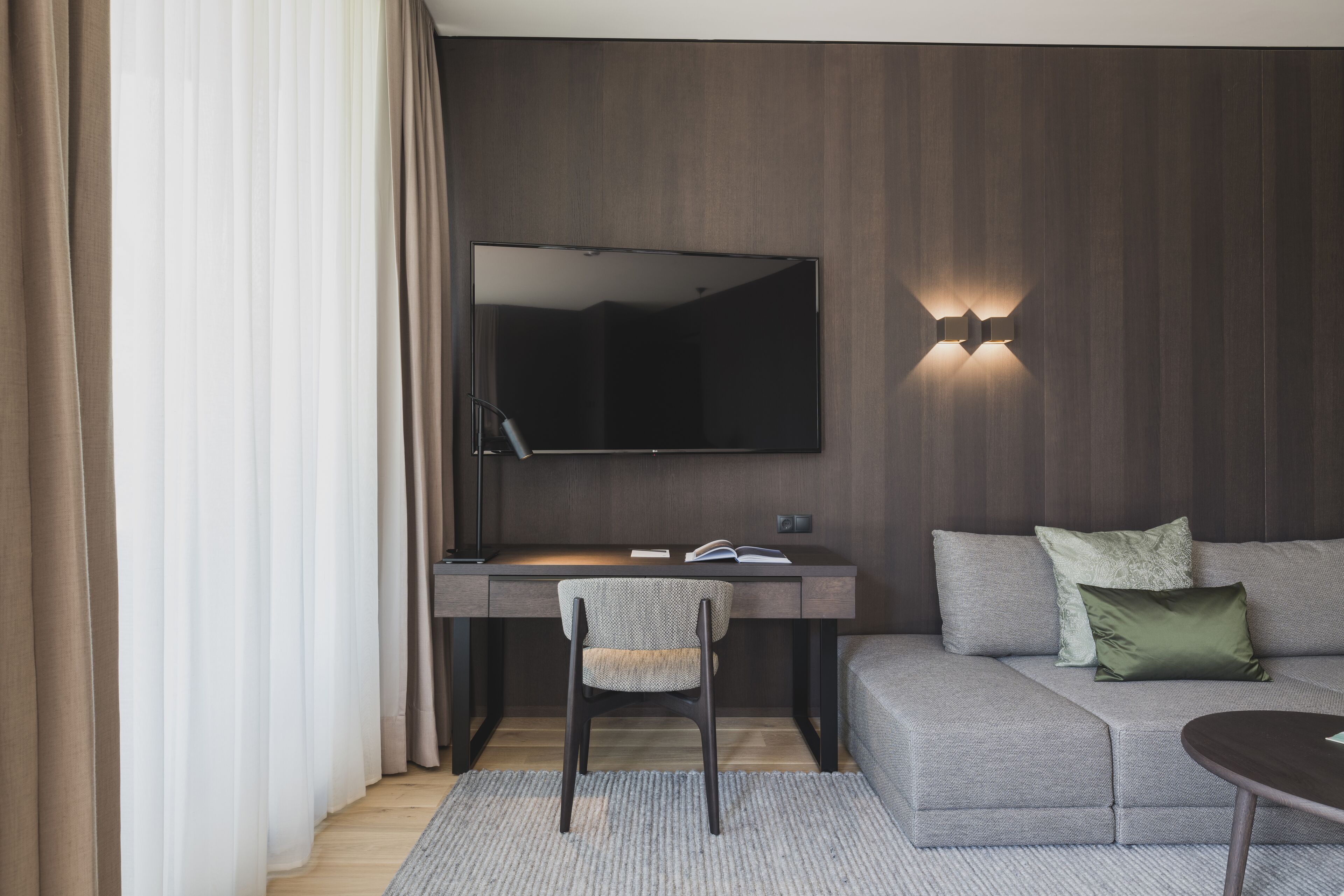 A modern room with a desk, chair, and a large flat-screen TV mounted on the wall.