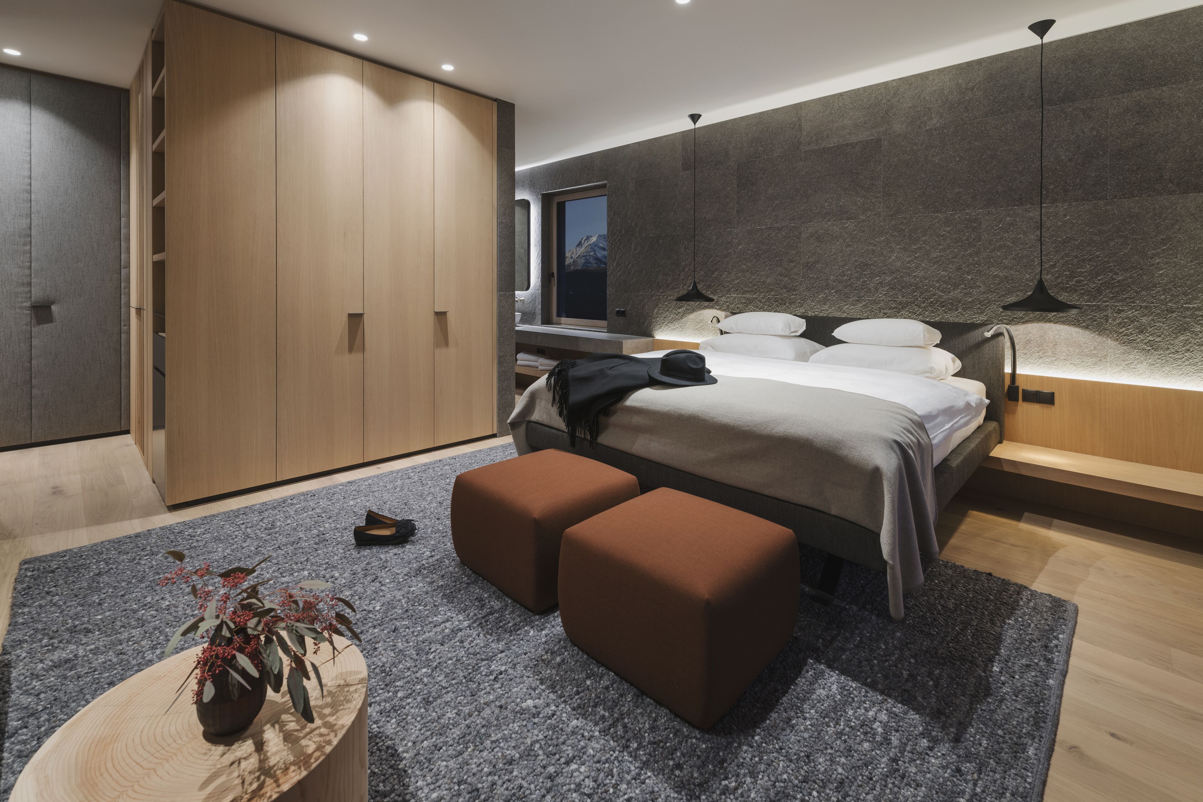 Un dormitorio moderno con cama, armario de madera y vistas a montañas a través de la ventana.