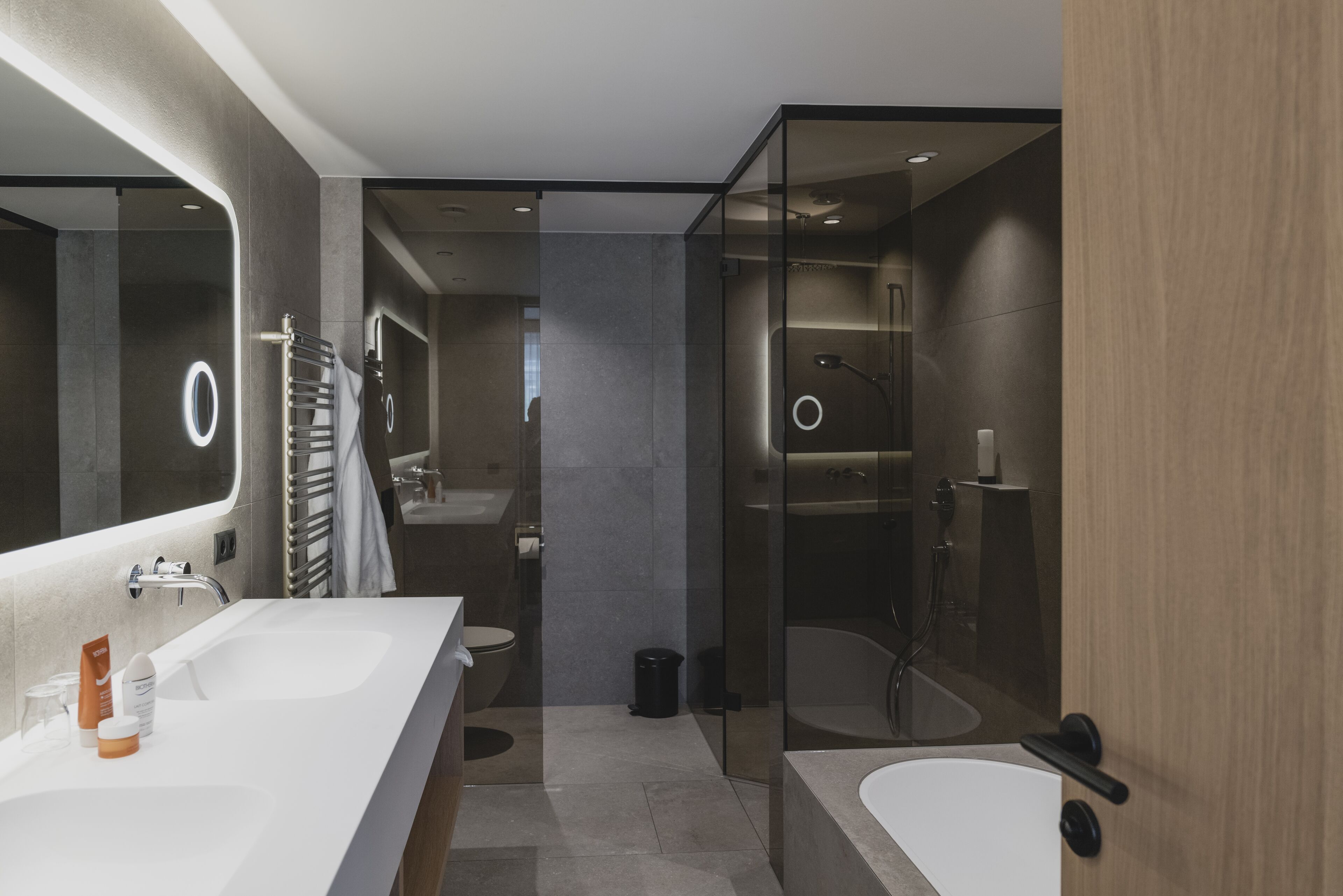 Un baño moderno con un espejo grande, dos lavamanos, una bañera y una zona de ducha con mampara de vidrio.